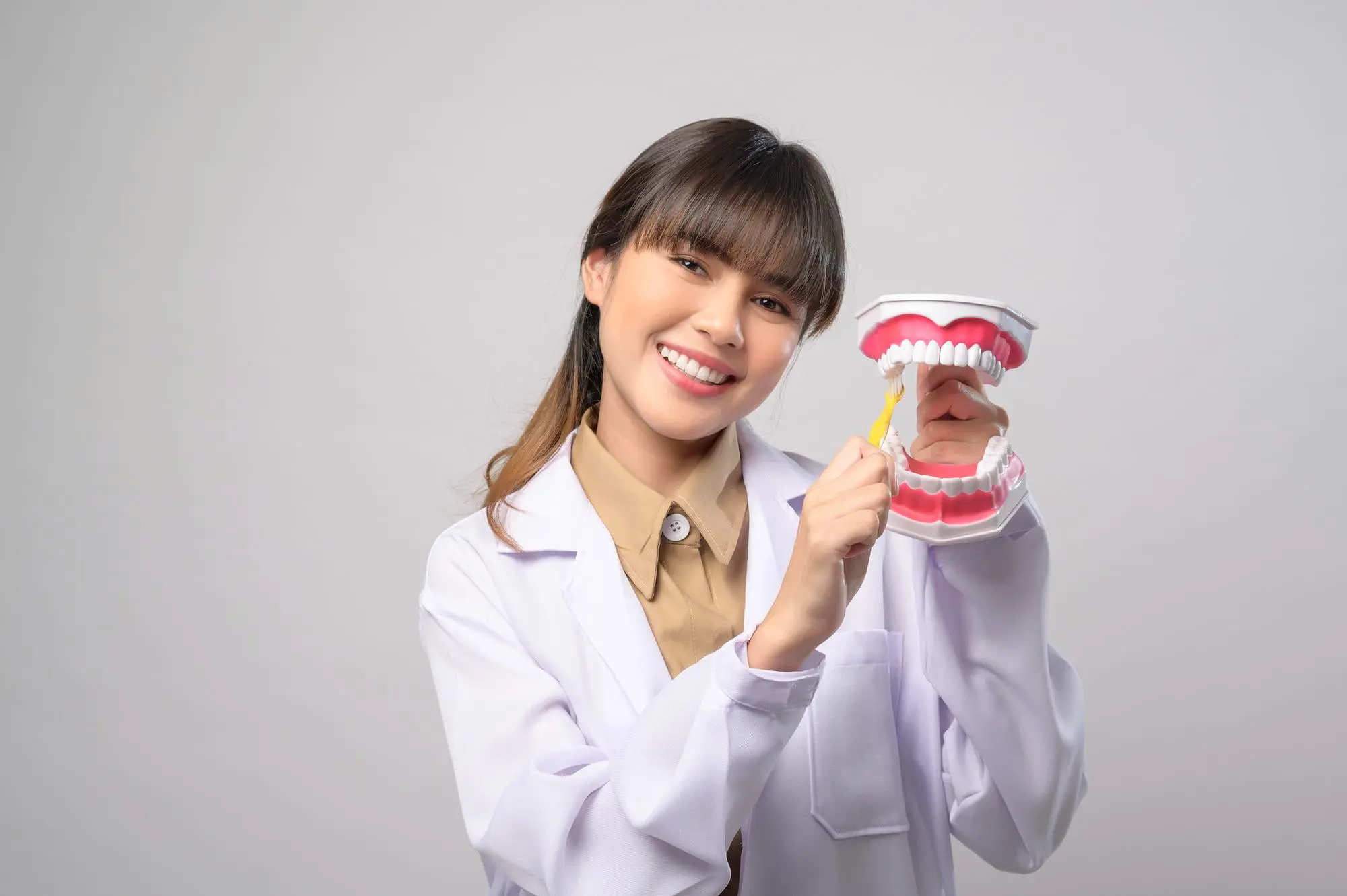A person in a lab coat at Sweet Smiles Orthodontics in Arlington, MA, shows how to brush braces using a toothbrush and dental model.