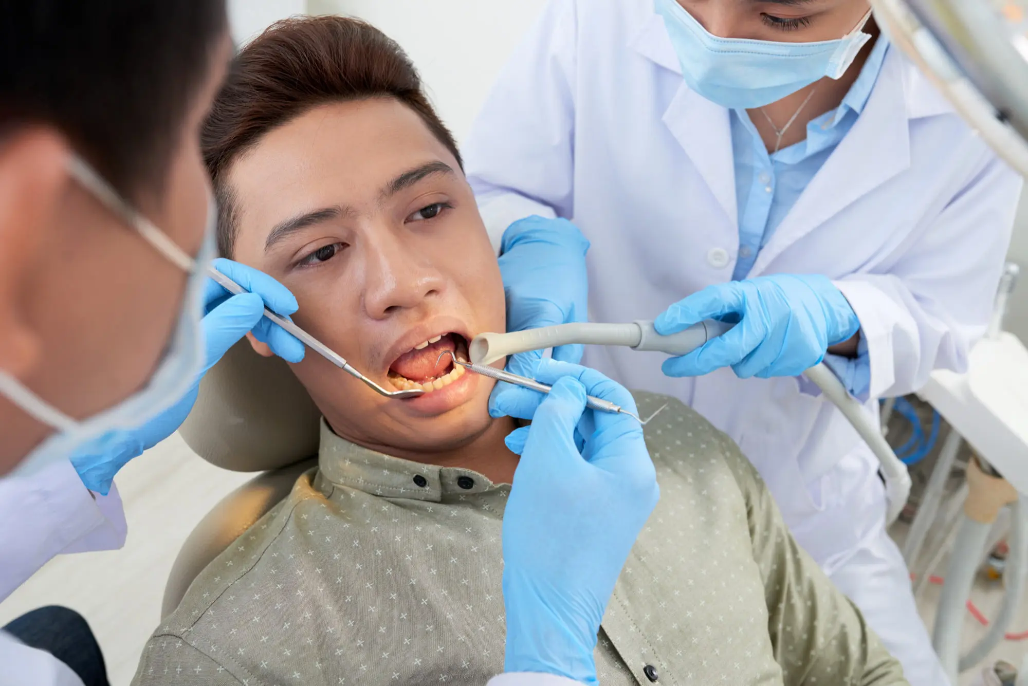 Male patient receiving professional braces examination from masked orthodontist and dental assistant using specialized instruments in clinical setting at Sweet Smiles Orthodontics in Arlington MA, demonstrating comprehensive orthodontic care and treatment after dental care for braces.