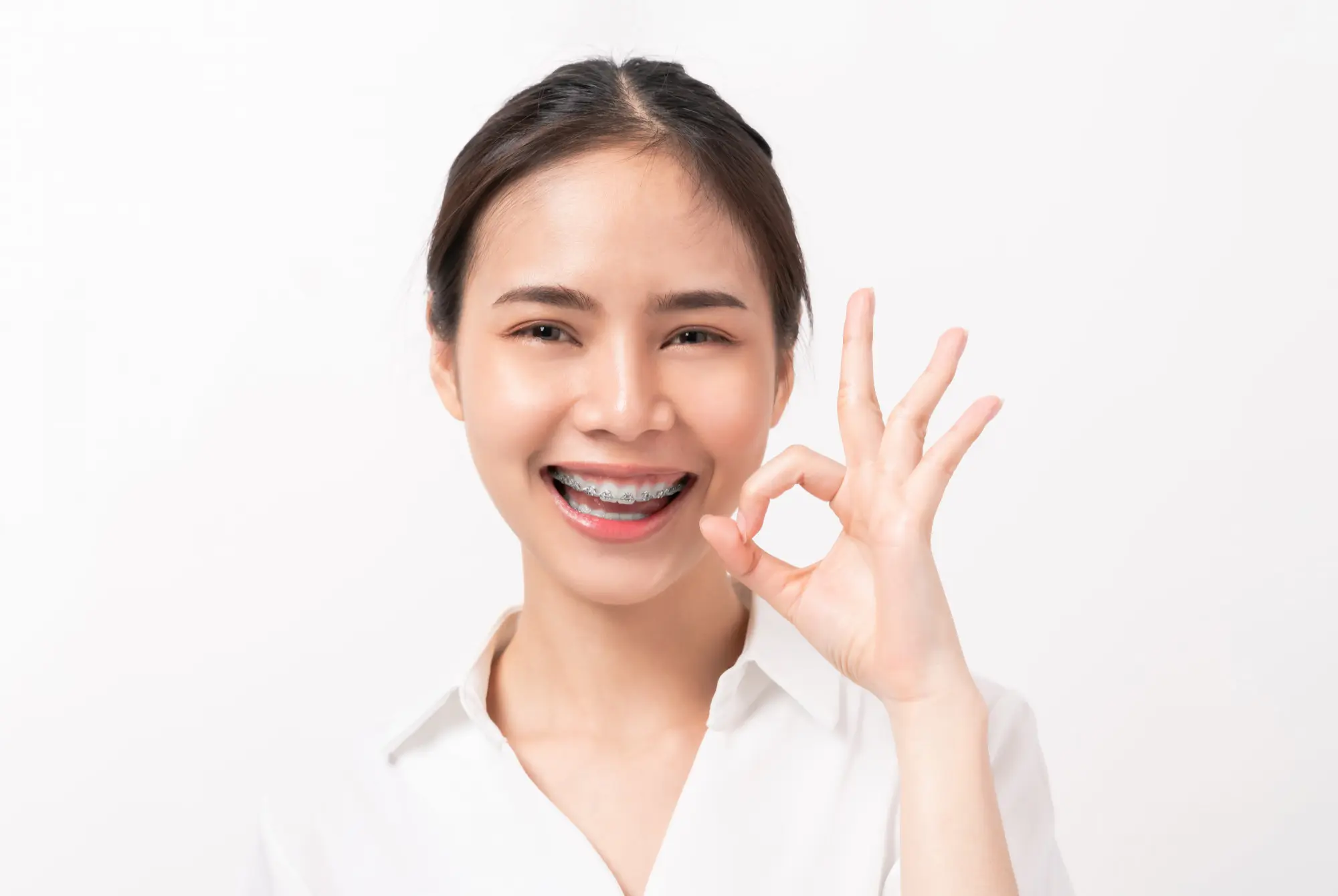 Sweet Smiles Orthodontics Arlington - Braces & Invisalign Confident young woman with metal braces making an 'OK' hand gesture and smiling brightly, demonstrating excellent value and patient satisfaction with affordable braces cost treatment at Sweet Smiles Orthodontics in Arlington, MA