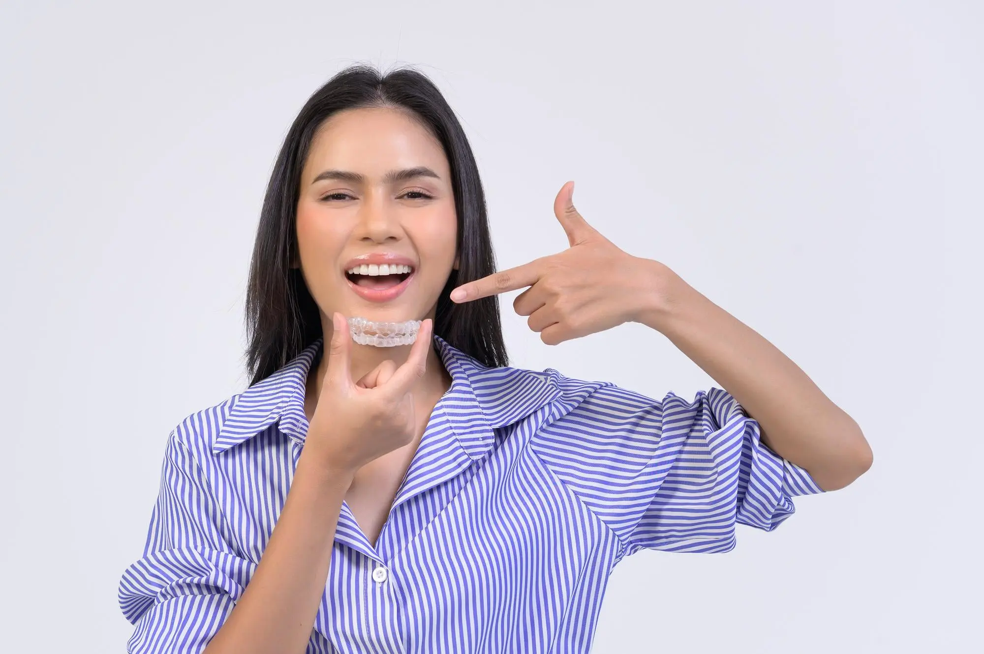 A woman in a striped shirt smiles and points to an Cheap Invisalign aligner from Sweet Smiles Orthodontics in Arlington, MA.