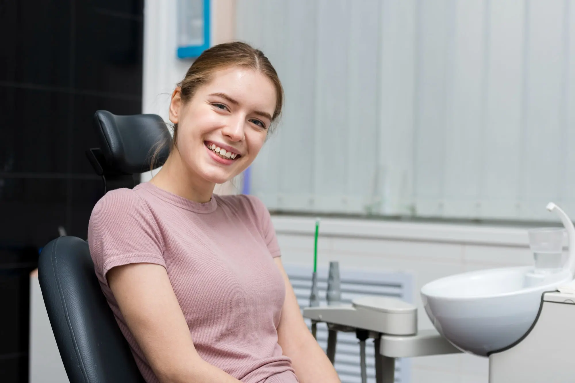 Smiling teenage patient with braces sits comfortably in dental chair showing progress in overbite correction treatment at Sweet Smiles Orthodontics in Arlington MA, with modern orthodontic equipment visible in clean, professional treatment room