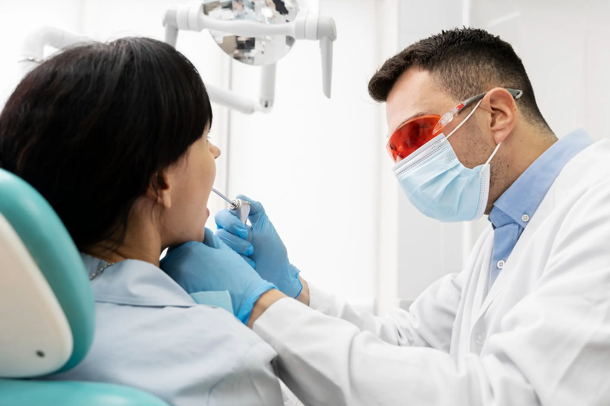 At Sweet Smiles Orthodontics in Arlington, MA, a masked dentist with protective glasses examines a patient's metal braces.