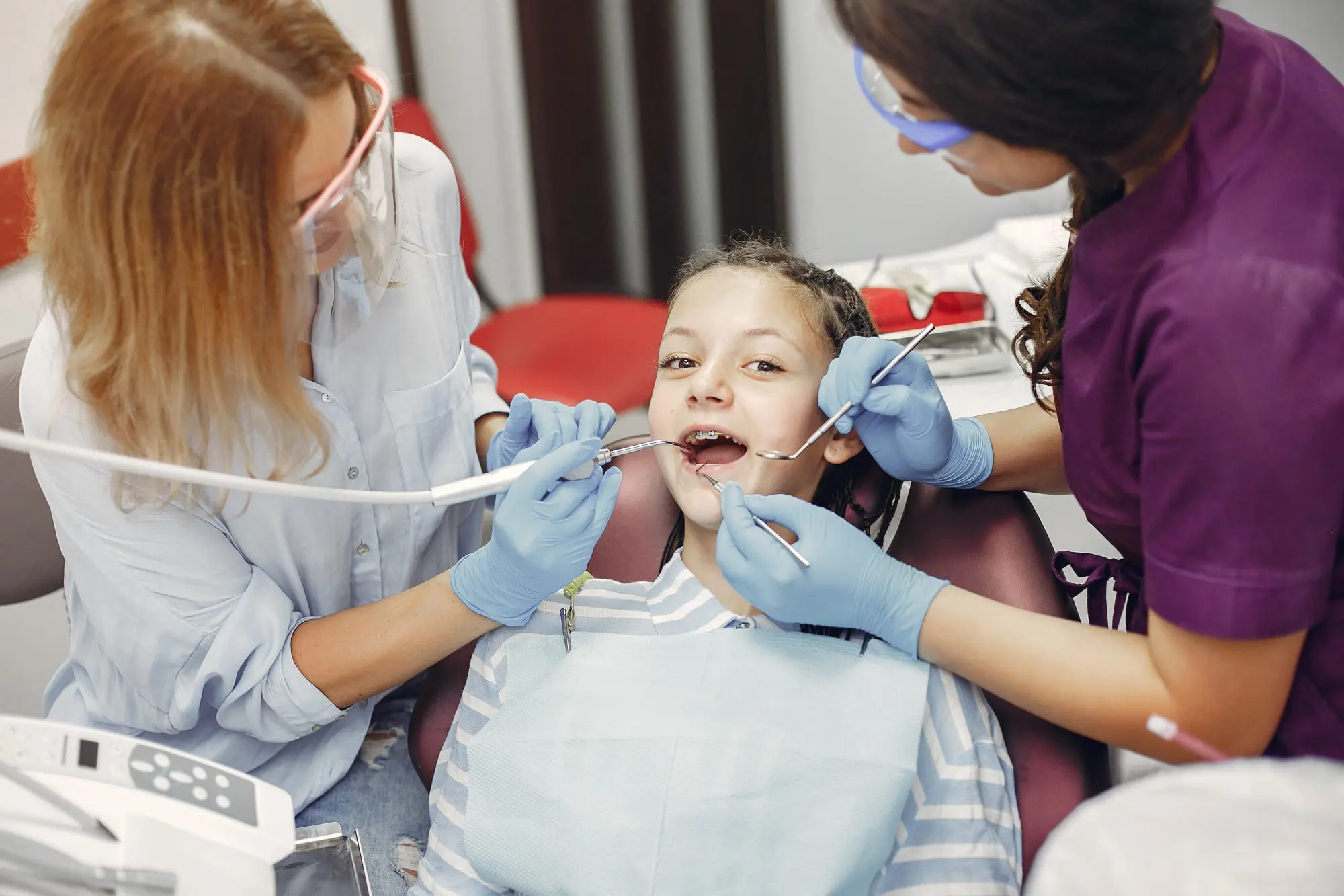 Two female dental professionals examining young patient's teeth with dental instruments during children's orthodontic treatment at Sweet Smiles Orthodontics in Arlington, MA