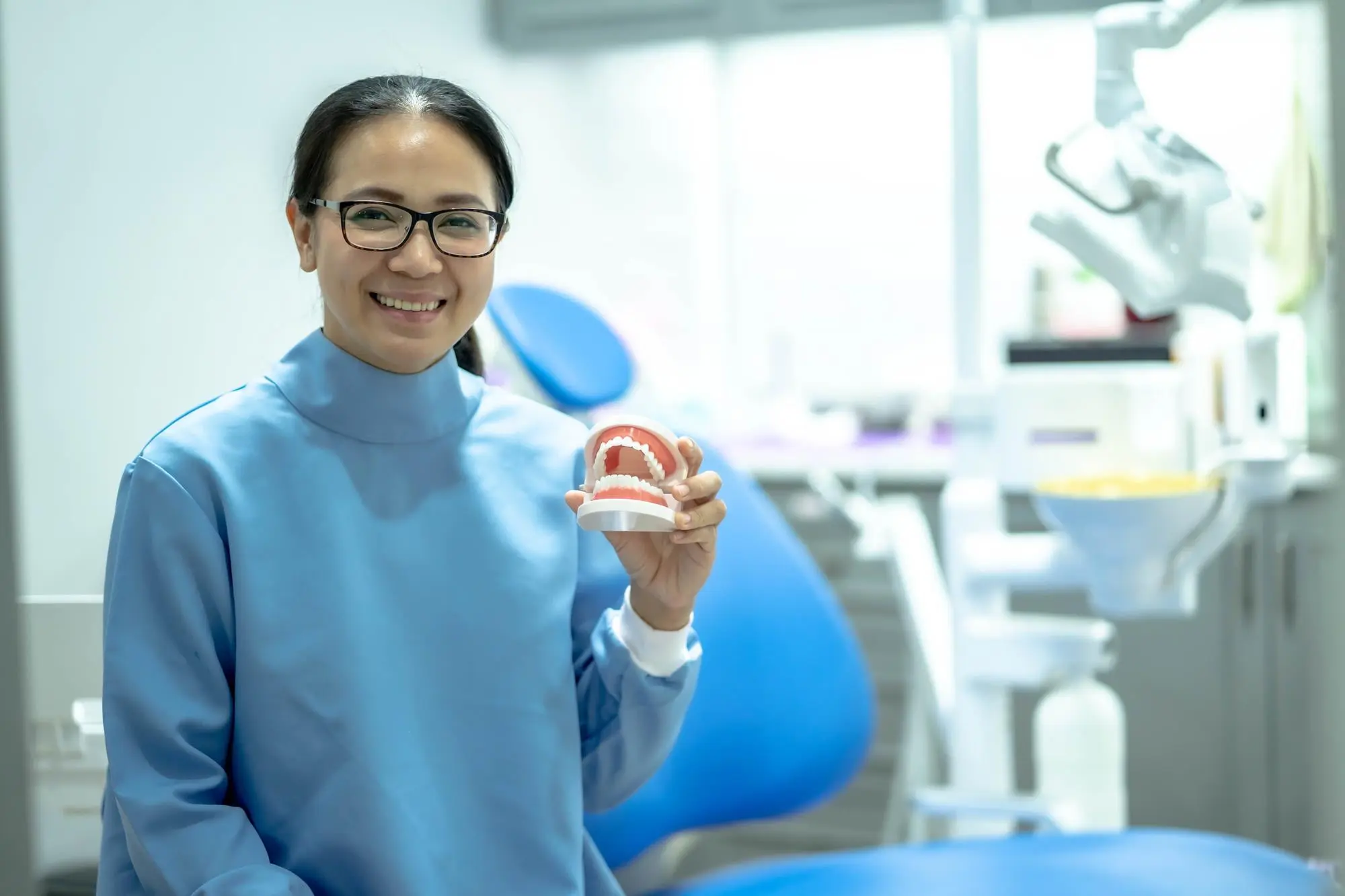 In Arlington, MA, a woman in glasses and blue lab coat at Sweet Smiles Orthodontics smiles holding a dental model.