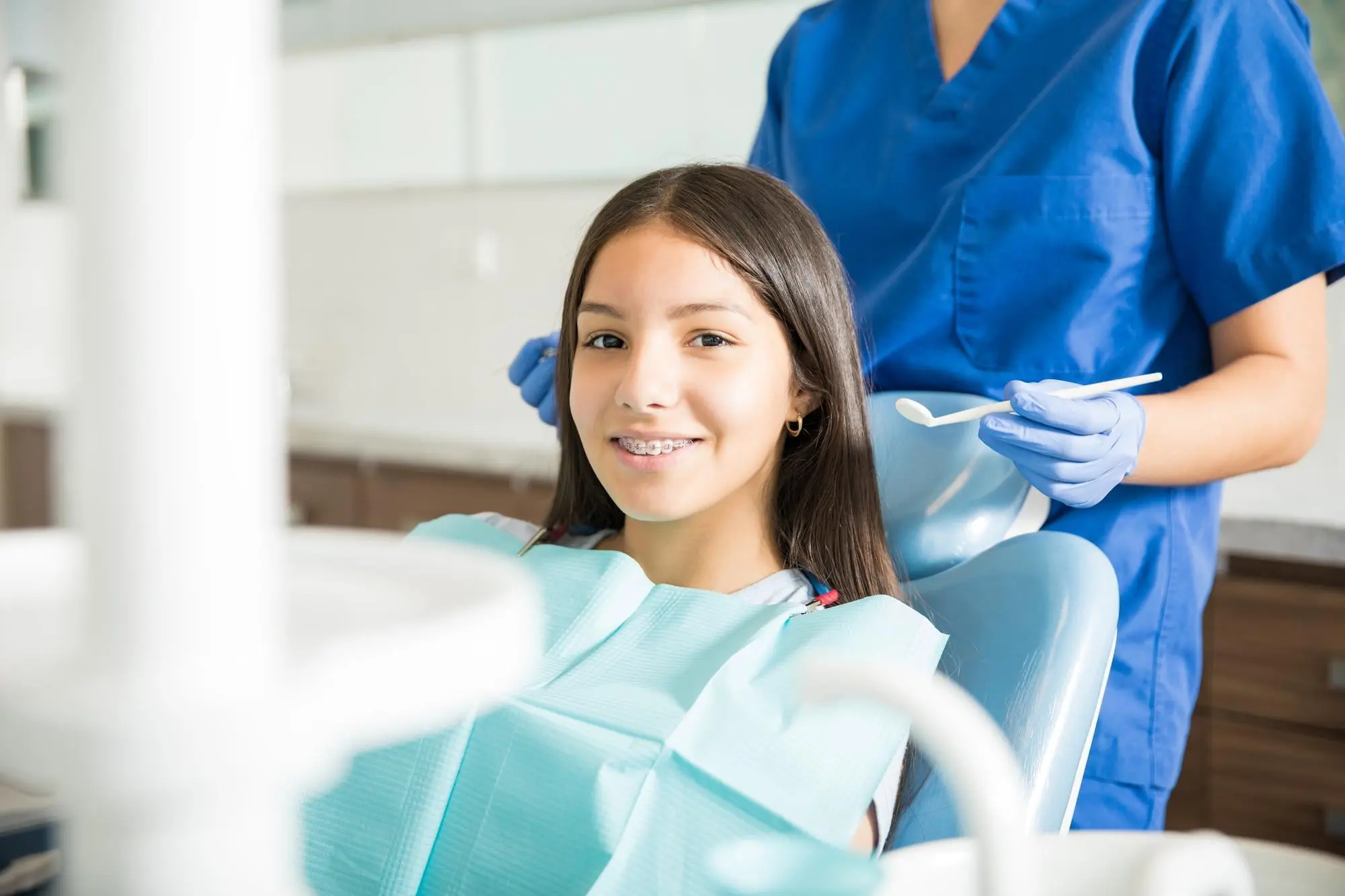 Young patient with braces smiles confidently during orthodontic consultation for mouth breathing correction, with dental professional in blue scrubs providing specialized care at Sweet Smiles Orthodontics in Arlington, MA