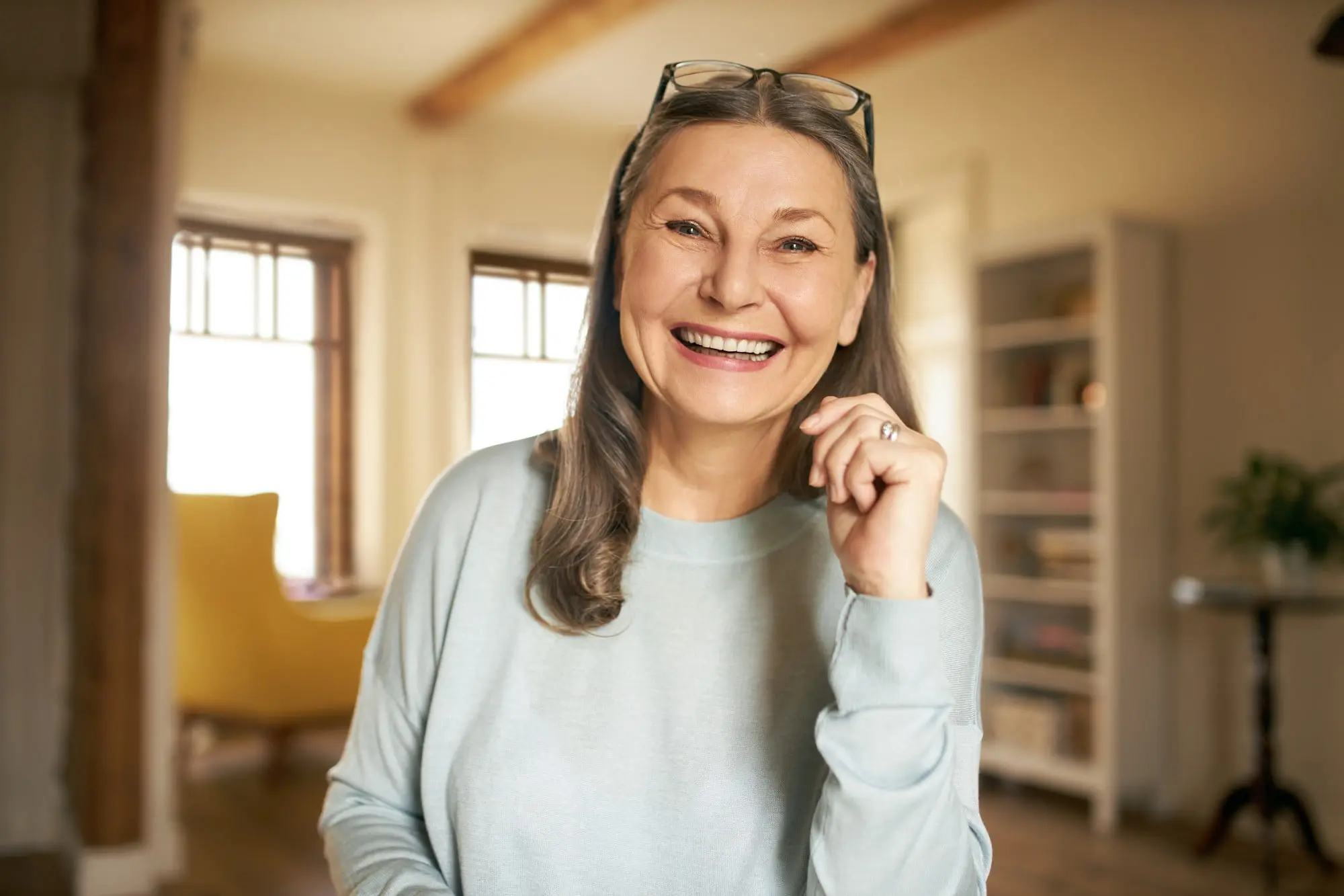 An older woman smiles represent orthodontic insurance plans at Sweet Smiles Orthodontics in Arlington, MA, with long gray hair, glasses, bookshelves, and big windows.