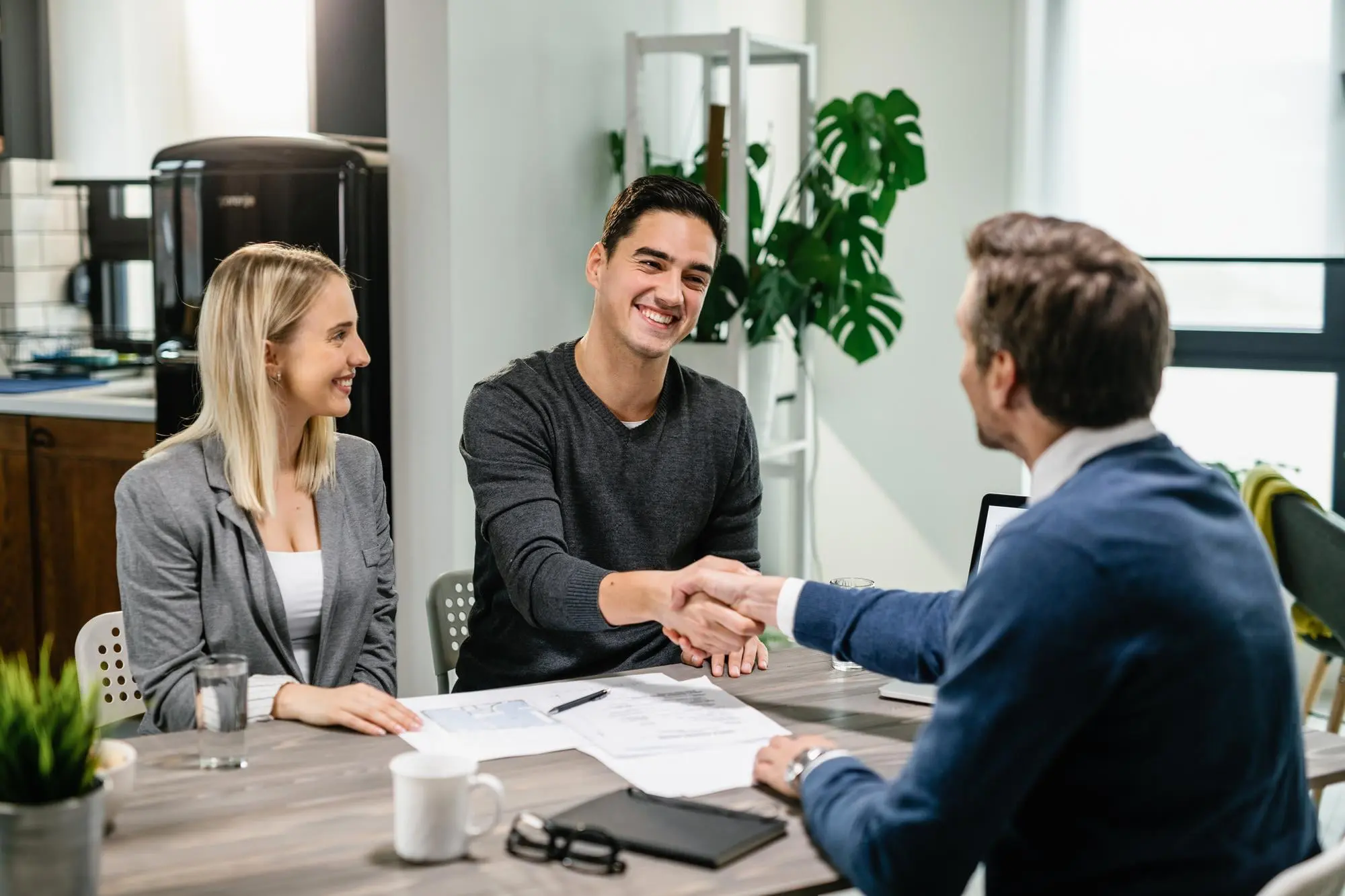 At Sweet Smiles Orthodontics in Arlington MA, two men shake hands at a table with documents as a woman smiles during an Invisalign payment plan meeting.