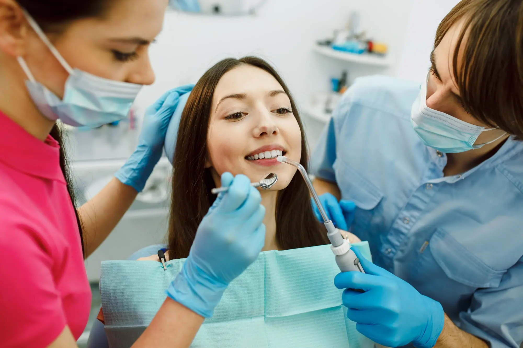 At Sweet Smiles Orthodontics in Arlington, MA, two masked dental professionals examine a woman's teeth, reviewing adult orthodontic options.