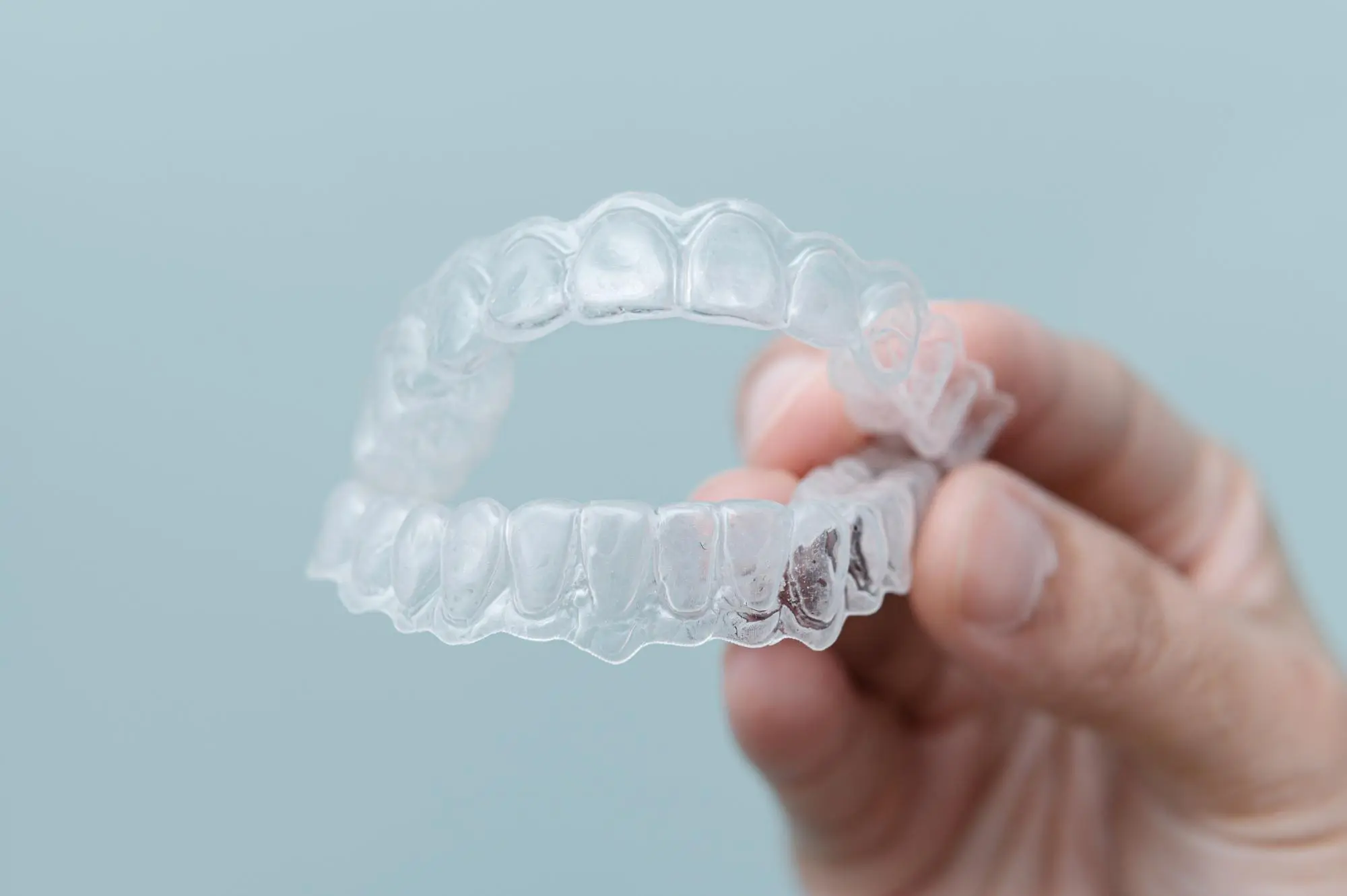 A hand displays a clear aligner against a light blue backdrop at Sweet Smiles Orthodontics in Arlington, MA.