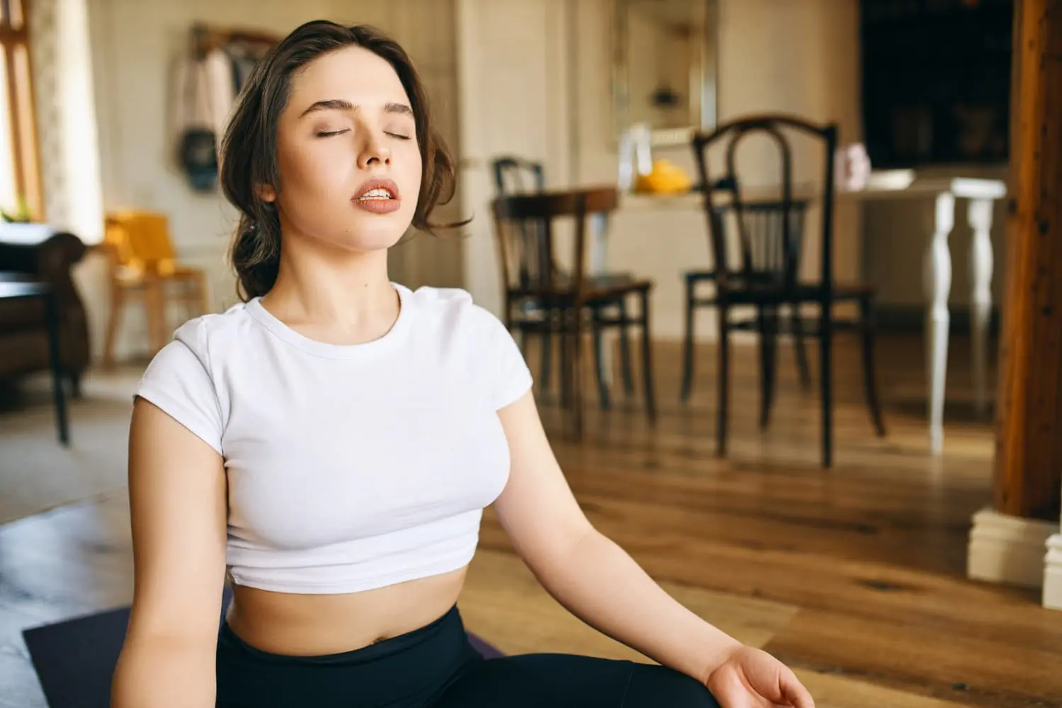 On a yoga mat indoors, a woman meditates in a white crop top—mindful mouth breathing at Sweet Smiles Orthodontics in Arlington, MA.