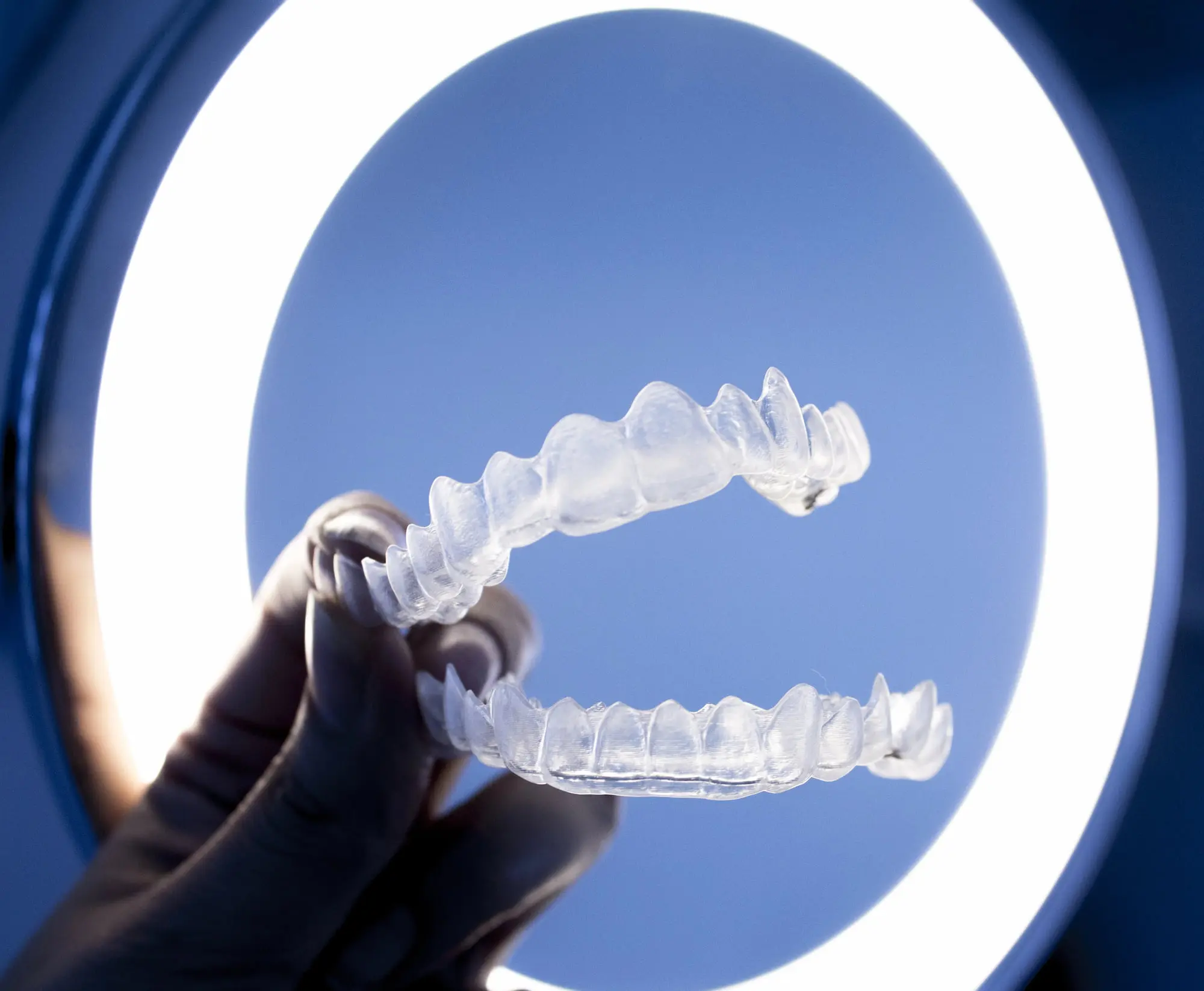 Professional orthodontic presentation of upper and lower Invisalign clear aligners held by gloved hand, representing quality treatment made accessible through flexible payment plan options at Sweet Smiles Orthodontics in Arlington, MA