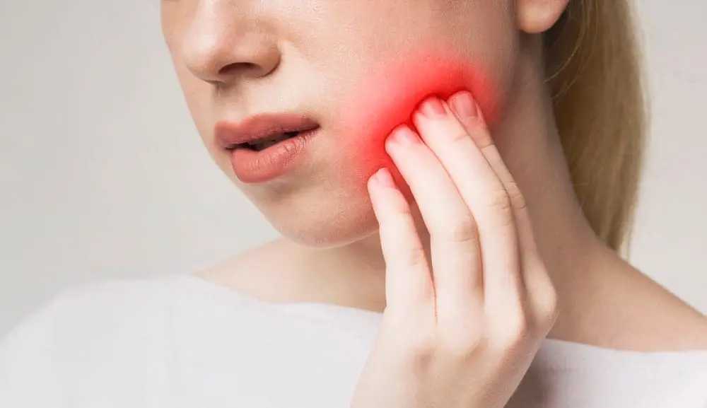 Woman holding her jaw in discomfort with red overlay indicating tooth pain, illustrating dental issues that can be addressed with Invisalign or braces treatment at Sweet Smiles Orthodontics in Arlington, MA