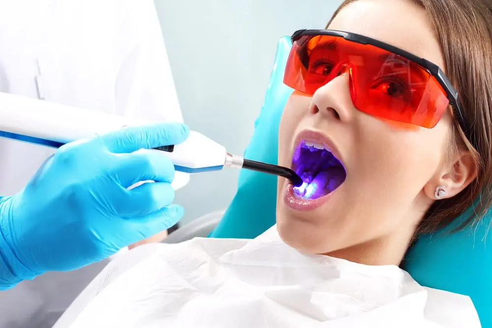 Female patient wearing protective eyewear during dental light treatment procedure at orthodontic office, demonstrating advanced technology used alongside Invisalign and braces treatments at Sweet Smiles Orthodontics in Arlington, MA