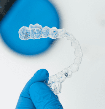 A gloved hand holds a clear Invisalign aligner, showcasing Sweet Smiles Orthodontics in Arlington, MA with flexible payment plans.
