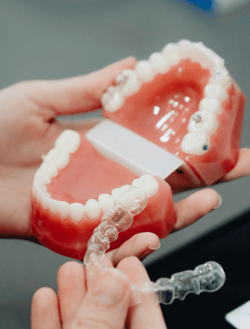 Hands holding dental model and clear Invisalign aligner during orthodontic consultation, representing flexible payment plan options that make Invisalign treatment accessible at Sweet Smiles Orthodontics in Arlington, MA