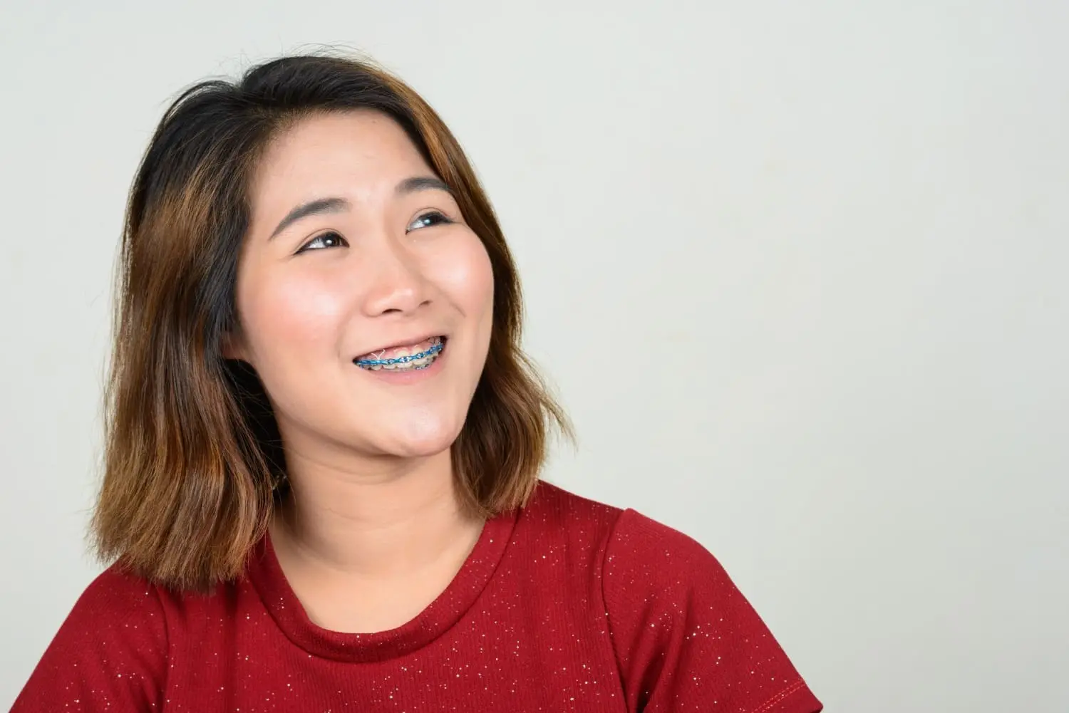 Happy young woman with blue braces looking upward with an optimistic expression, showcasing the confidence and positive outlook that comes with adult braces at Sweet Smiles Orthodontics in Arlington, MA
