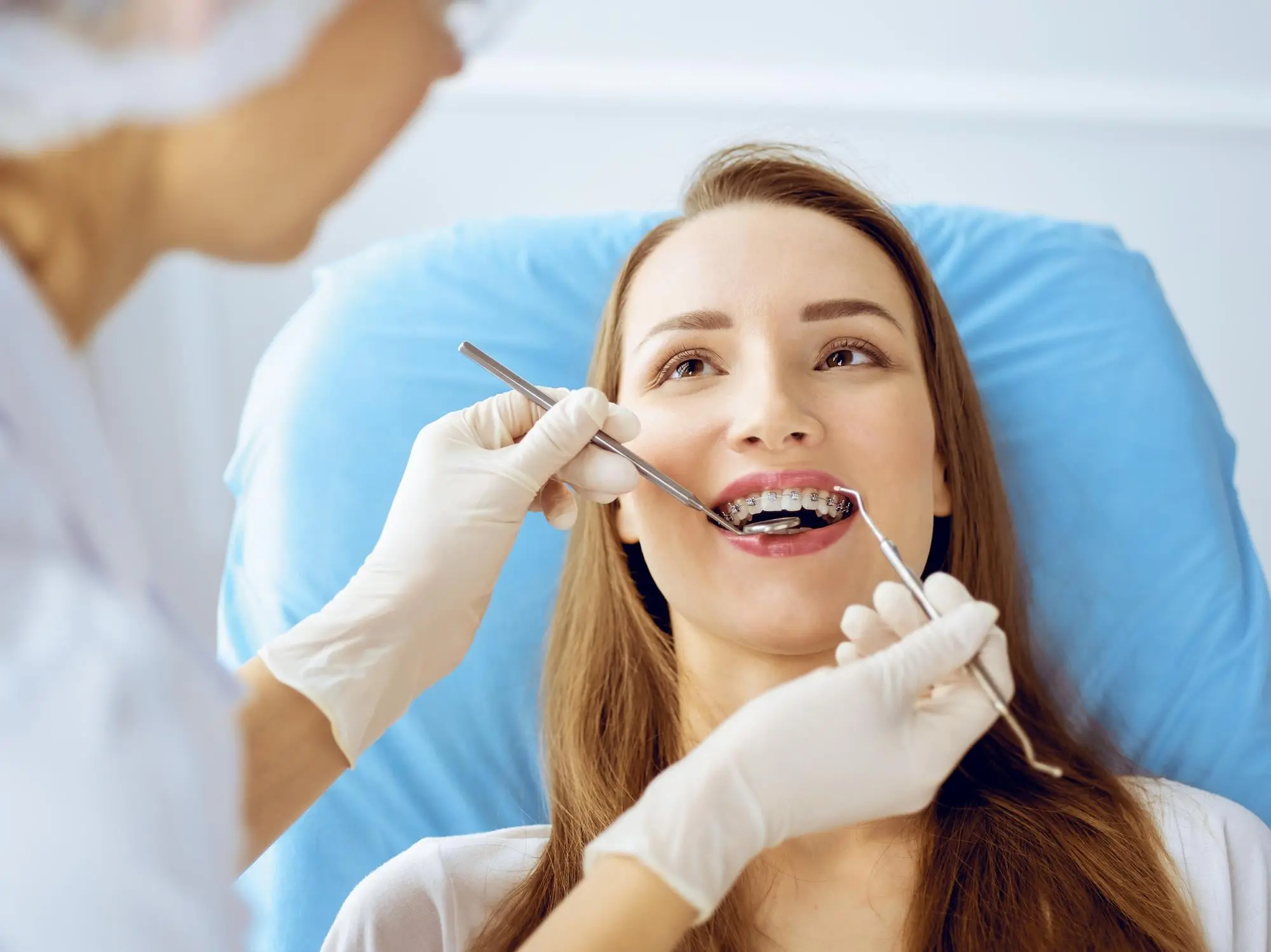 A dentist examines a woman with braces for overbite treatment at Sweet Smiles Orthodontics in Arlington, MA, as she sits in a dental chair.