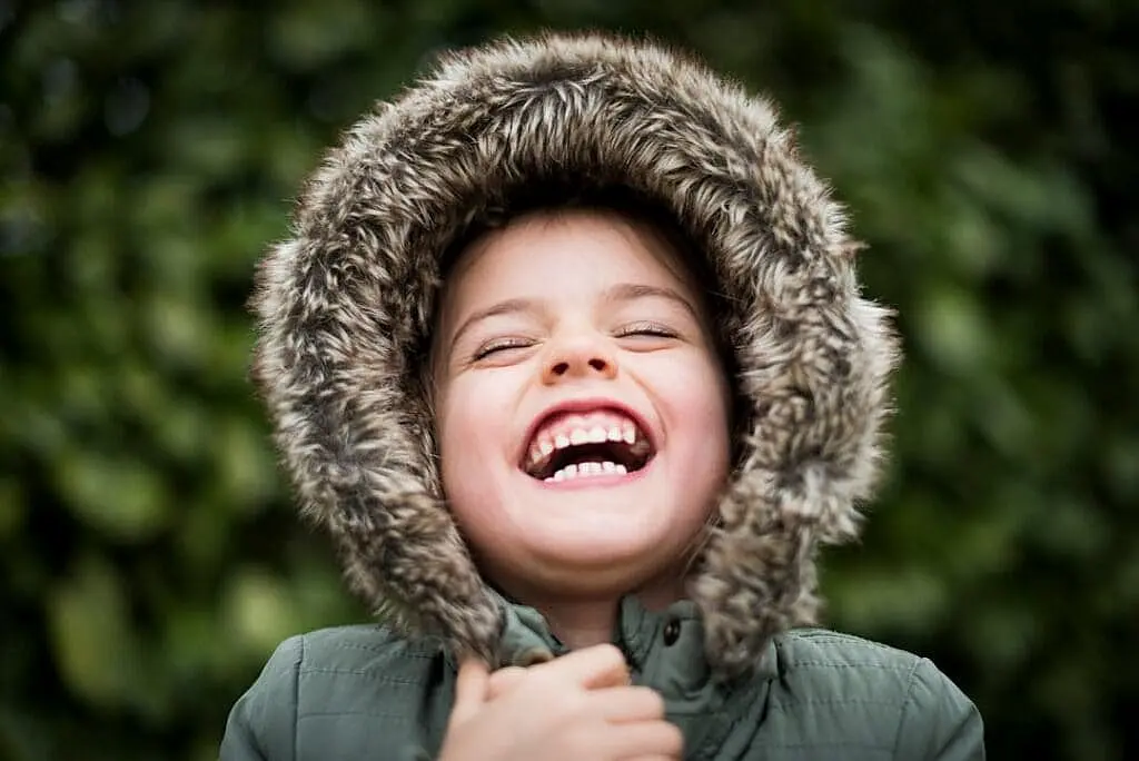Joyful child with a bright, wide smile wearing a fur-trimmed winter hood outdoors, representing the happy, confident smiles achieved through affordable orthodontic treatment at Sweet Smiles Orthodontics in Arlington, MA