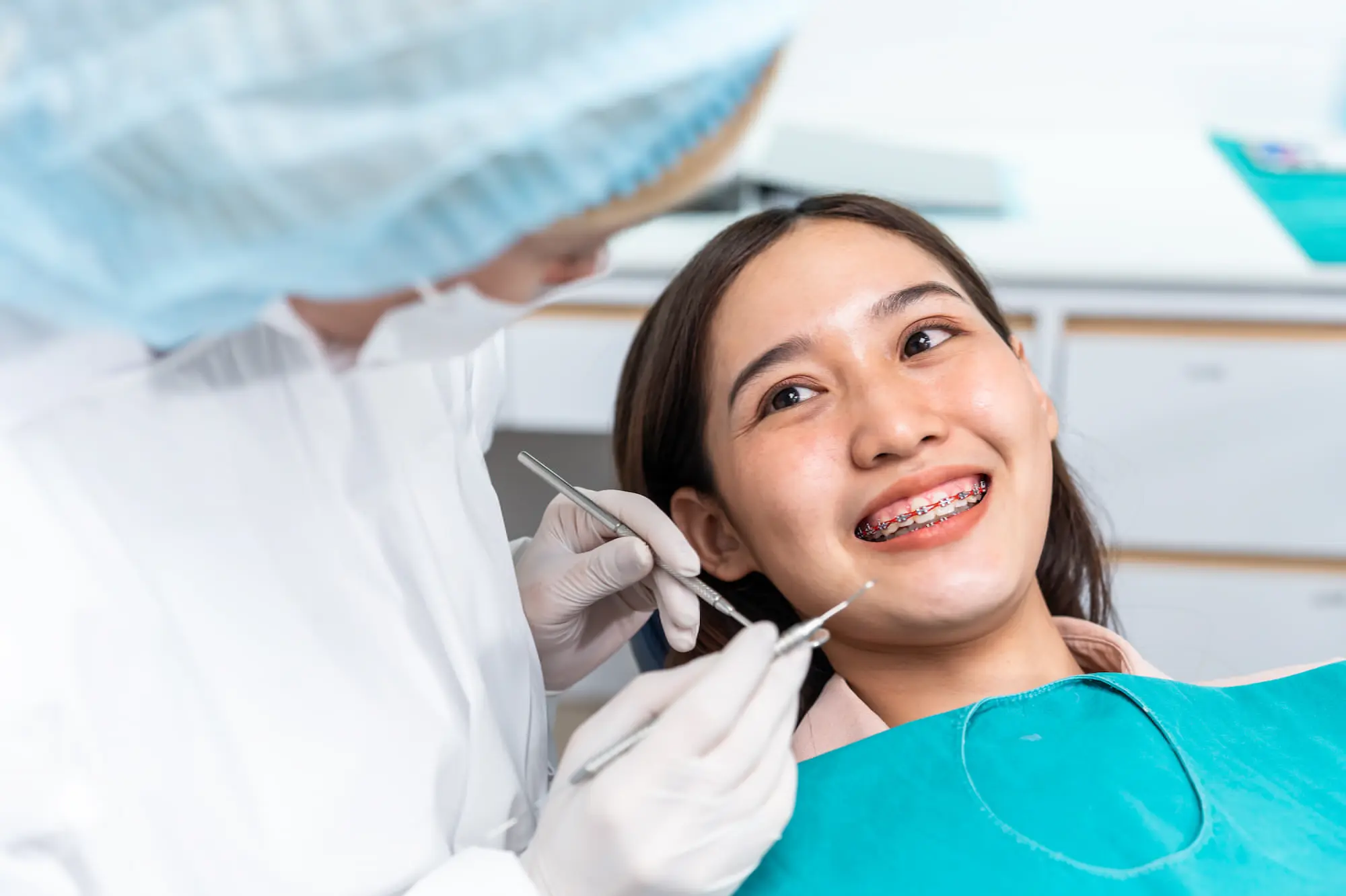A dentist at Sweet Smiles Orthodontics in Arlington, MA checks a smiling braces patient reclined in a chair with a bib.