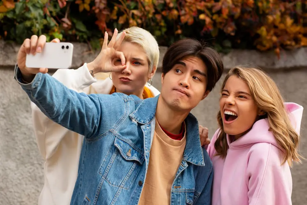 Friends take a selfie outdoors after consider type of braces from Sweet Smiles Orthodontics in Arlington, MA; one winks, another makes an OK sign.