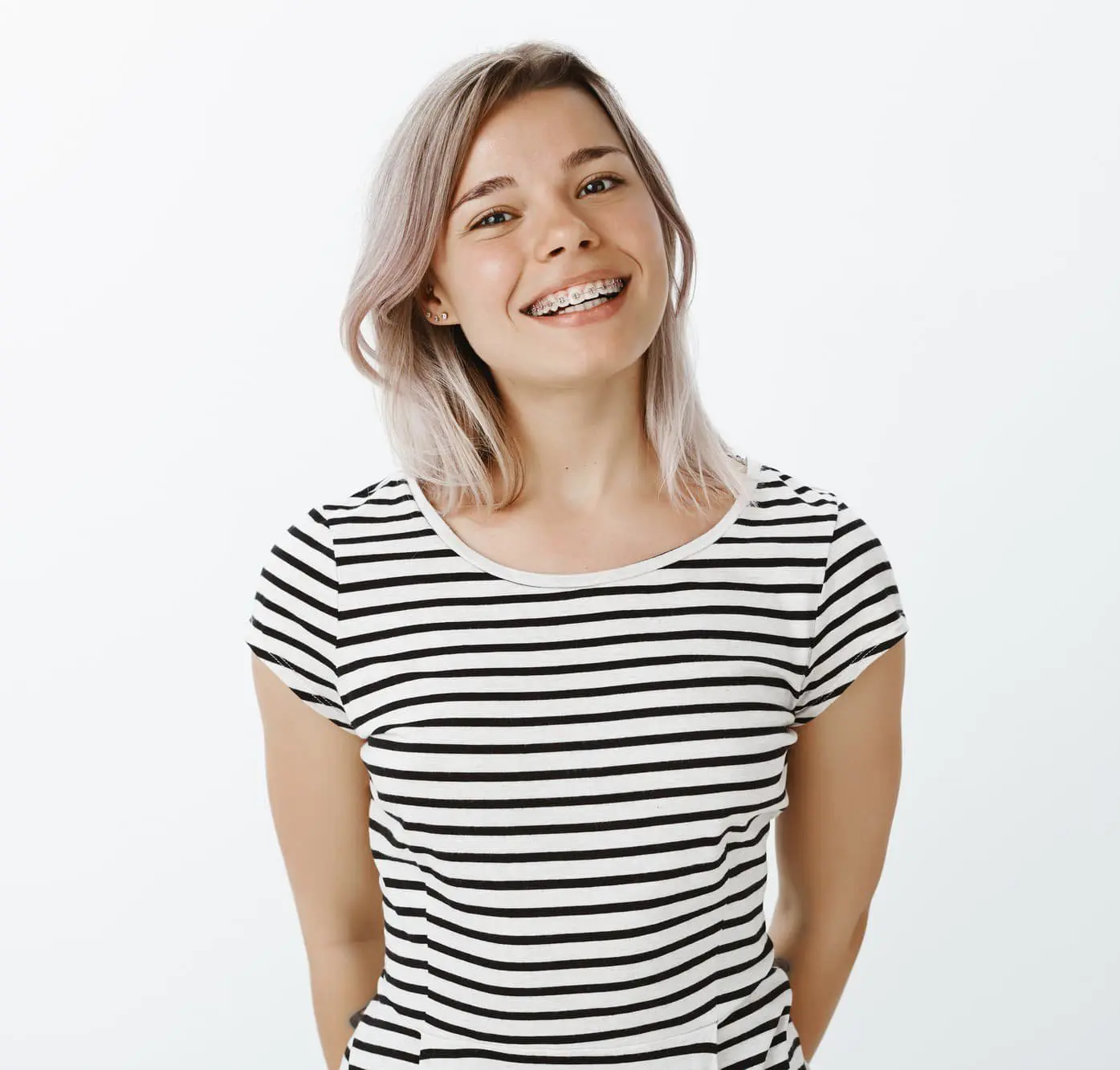 A smiling young woman with braces, a striped shirt, and light hair after considering Invisalign vs Braces at Sweet Smiles Orthodontics in Arlington, MA.