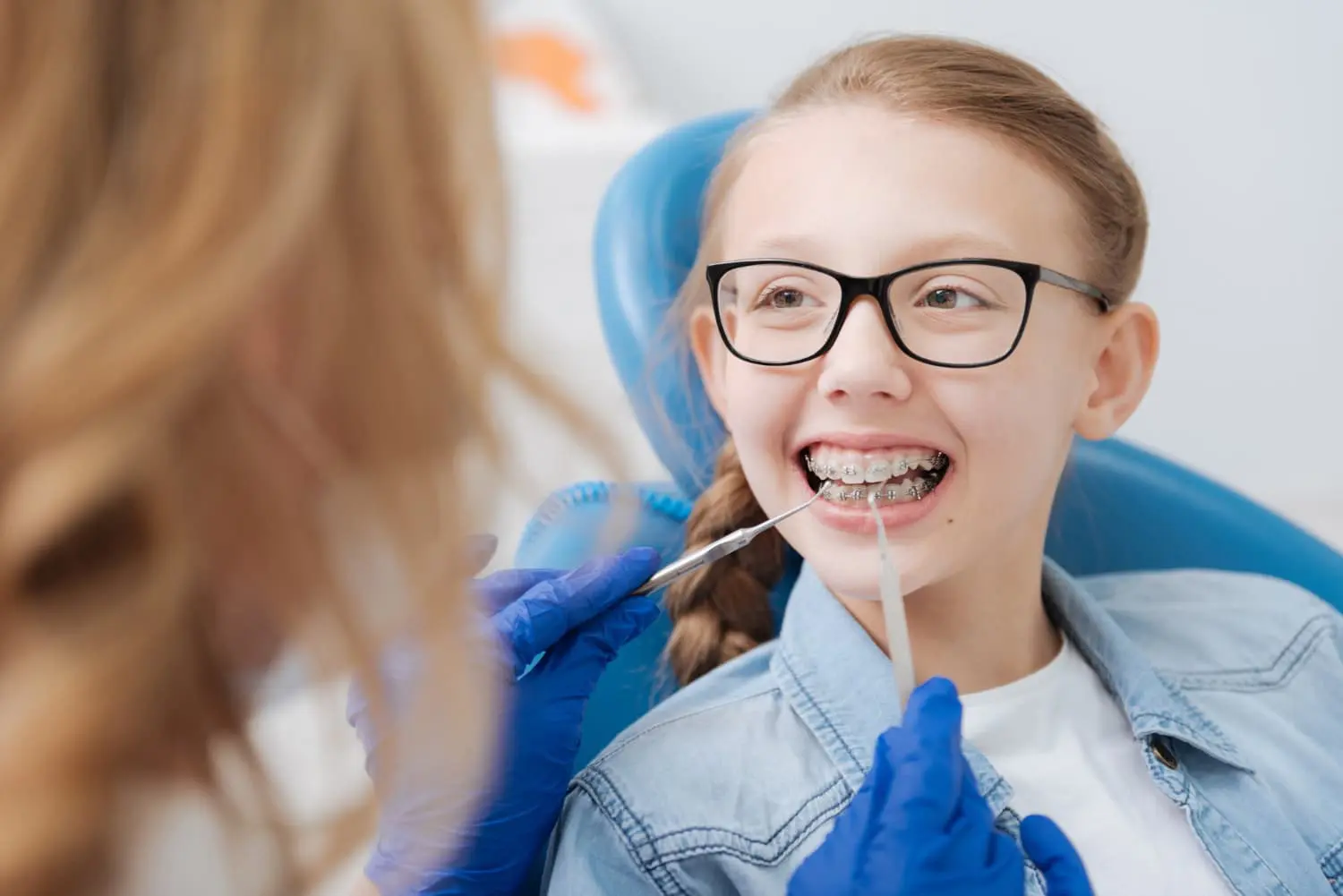 At Sweet Smiles Orthodontics in Arlington, MA, a girl with braces smiles in a dental chair, representing the Importance of Early Orthodontic Intervention in dental care with Children’s orthodontists.