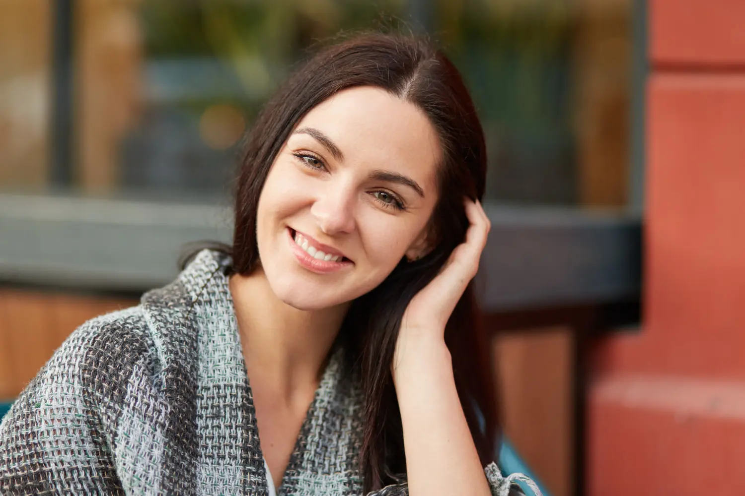 A woman smiles confidently at the camera, representing Sweet Smiles Orthodontics in Arlington, MA, with an urban backdrop.