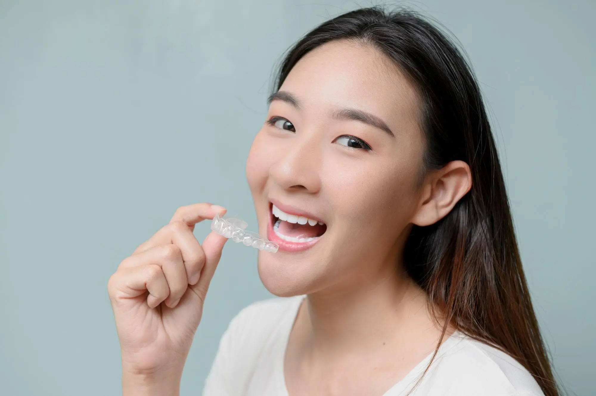 Smiling at the camera, a woman in Arlington, MA, holds a clear dental aligner, showcasing orthodontic coverage basics from braces at Sweet Smiles Orthodontics benefits.