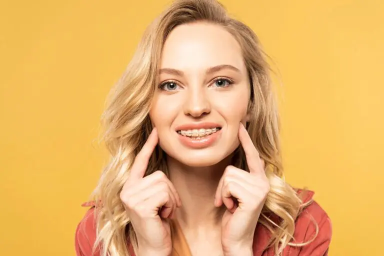 Smiling woman with blonde hair points to her metal braces, promoting Sweet Smiles Orthodontics in Arlington, MA, on yellow background.