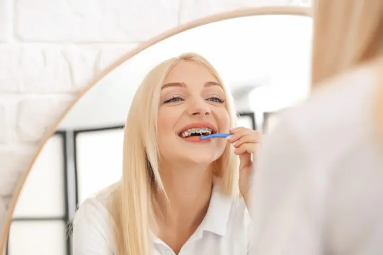 A woman with braces brushes her teeth in a bathroom mirror at Sweet Smiles Orthodontics in Arlington, MA, showing oral care - How To Floss With Braces in Arlington, MA