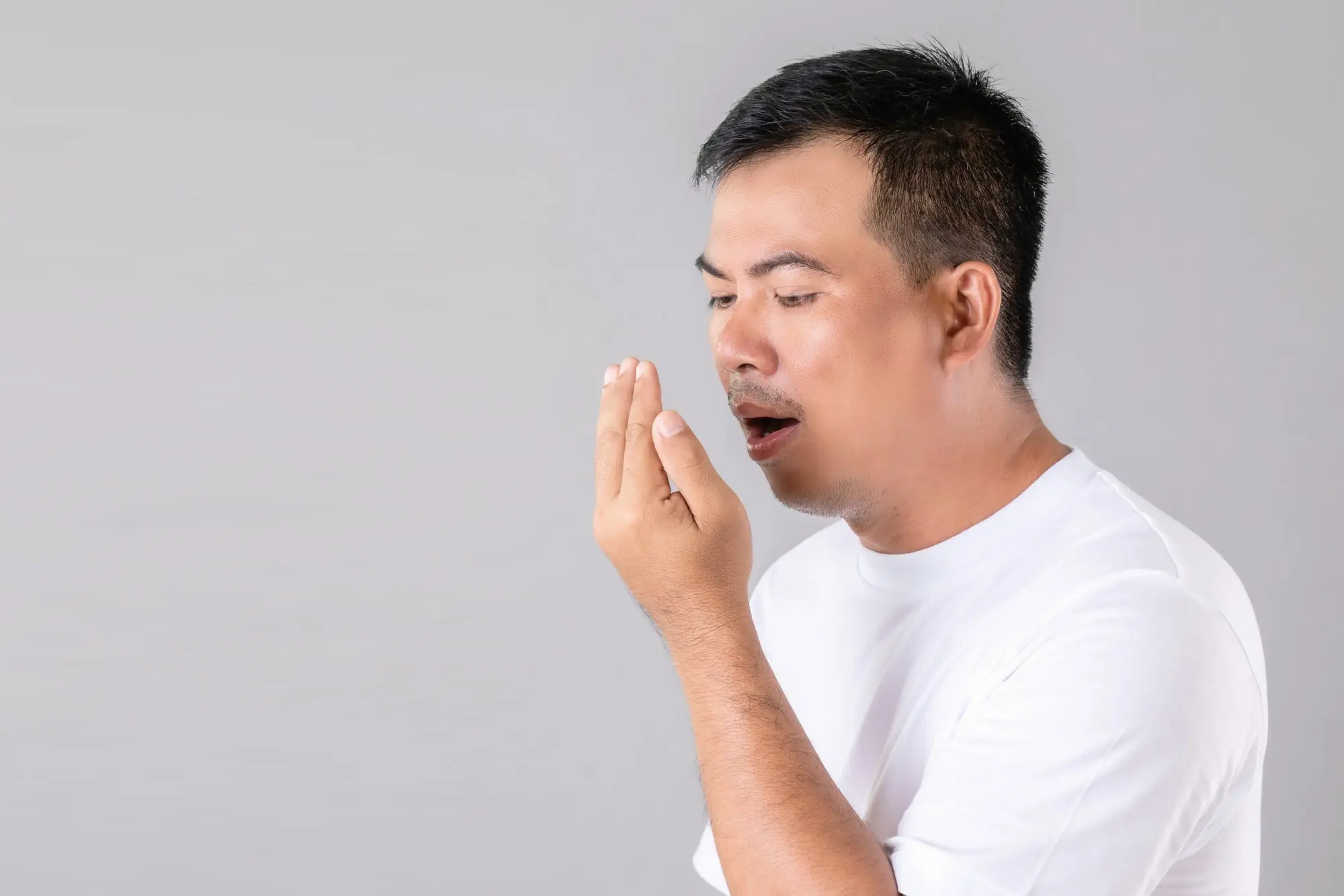 A man checks if he's a mouth breather by breathing into his hand, with Sweet Smiles Orthodontics in Arlington, MA branding shown.