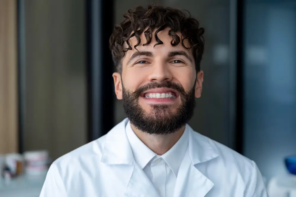 Smiling bearded man in a white lab coat at Sweet Smiles Orthodontics, ready to discuss braces alternatives in Arlington, MA - Alternatives to Braces in Arlington, MA