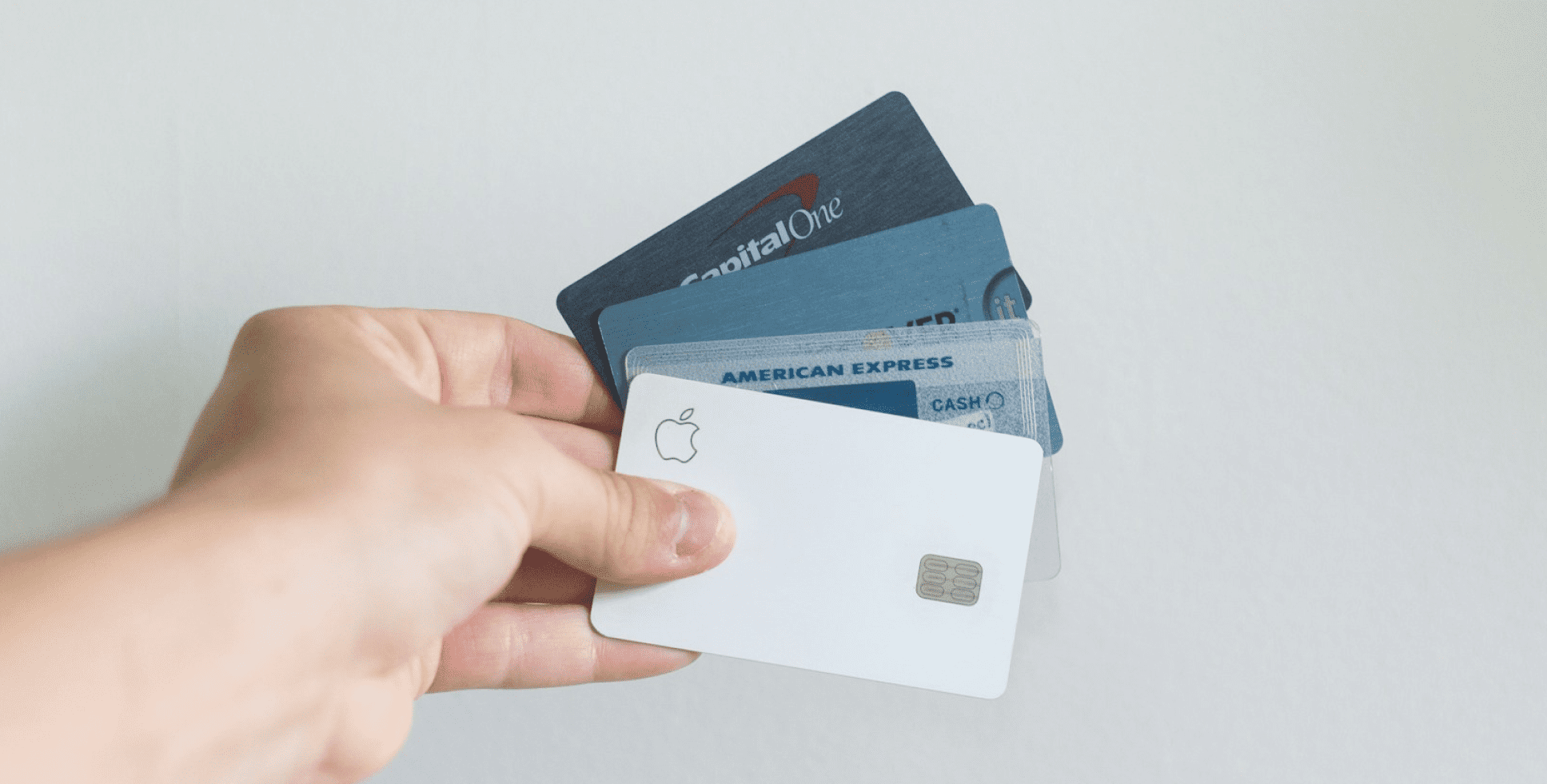 Hand holding multiple credit cards including Capital One, American Express, and Apple Card, representing the variety of payment methods accepted for flexible Invisalign payment plan at Sweet Smiles Orthodontics in Arlington, MA